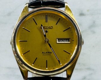 Reloj Seiko vintage con alarma de cuarzo, tono dorado, día y fecha, correa nueva de cristal.