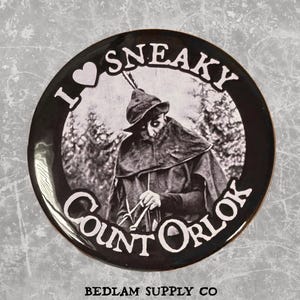 May include: A black and white button with the text "I <3 SNEAKY Count Orlok" and an image of Count Orlok from the film Nosferatu. The button has a glossy finish and a black border. The text "BEDLAM SUPPLY CO" is at the bottom.