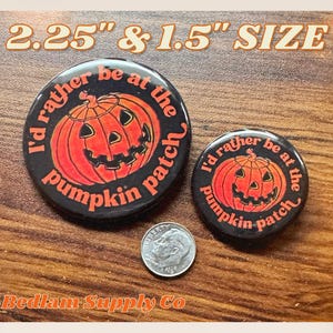K&ouml;nnte beinhalten: Zwei schwarze und orangefarbene Halloween-Anstecknadeln mit dem Text "I'd rather be at the pumpkin patch". Die gr&ouml;&szlig;ere Nadel hat einen Durchmesser von 2,25 Zoll und die kleinere einen Durchmesser von 1,5 Zoll.
