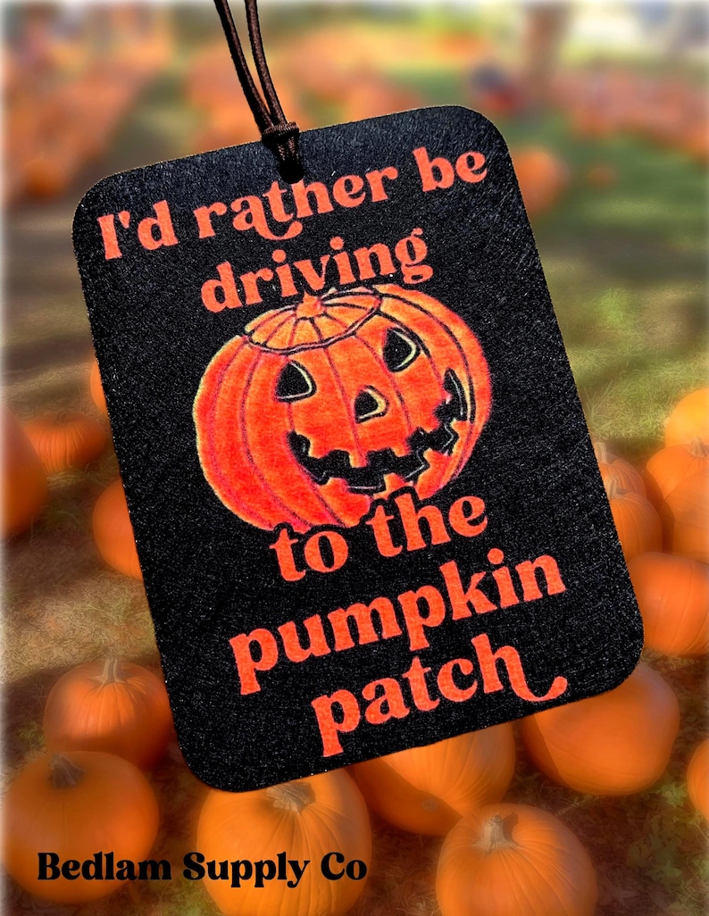 May include: A black car air freshener with a pumpkin illustration and the text 'I'd rather be driving to the pumpkin patch'.