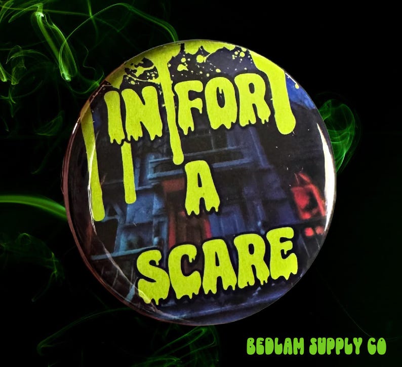 May include: Round button with the text "IN FOR A SCARE" in dripping neon green letters. The background features a spooky house illustration. The button has a glossy finish and is set against a black background with green smoke.