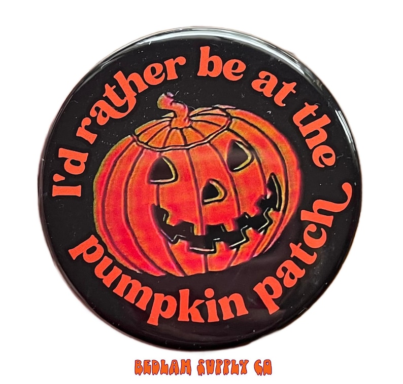 K&ouml;nnte beinhalten: Ein schwarzer Knopf mit dem Text "I'd rather be at the pumpkin patch" in orange. Ein orangefarbener Cartoon-K&uuml;rbis mit einem K&uuml;rbisgesicht befindet sich in der Mitte des Knopfes.