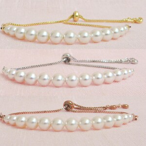 May include: Three pearl bracelets with adjustable sliding knots. The bracelets are shown on a pink background. The first bracelet has a gold chain, the second has a silver chain, and the third has a rose gold chain.