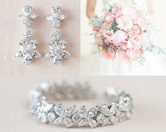 May include: A set of silver bridal earrings and a bracelet with crystal flower accents. The earrings are dangling and feature multiple flower shapes. The bracelet is a delicate band with a row of crystal flowers.