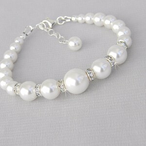 May include: A white pearl bracelet with a silver clasp and a small pearl charm. The bracelet features larger pearls with clear rhinestone accents.