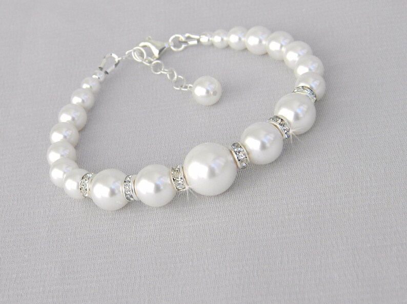 May include: A white pearl bracelet with a silver clasp and a small pearl charm. The bracelet features larger pearls with clear rhinestone accents.