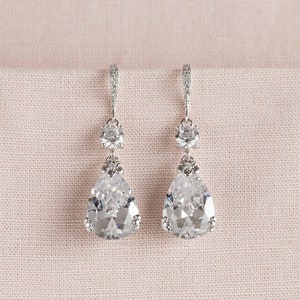 May include: A pair of silver teardrop earrings with clear crystal accents. The earrings feature a large teardrop-shaped crystal with smaller round crystals above it.