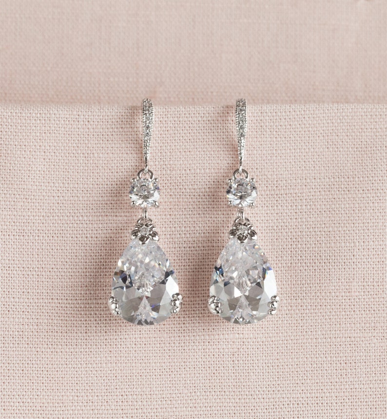 May include: A pair of silver teardrop earrings with clear crystal accents. The earrings feature a large teardrop-shaped crystal with smaller round crystals above it.