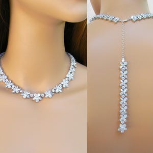 May include: A silver necklace with a delicate floral design. The necklace has a long, dangling back piece that can be worn as a back necklace.