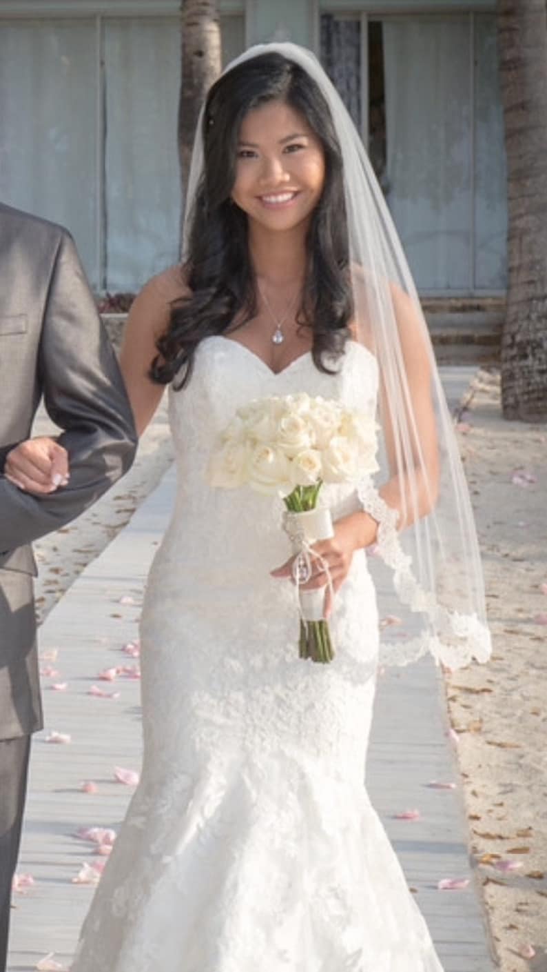 May include: A bride in a white lace wedding dress with a veil and a bouquet of white roses.