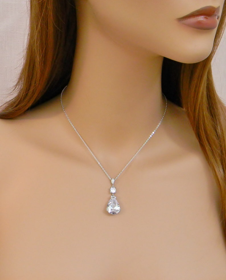 May include: A silver necklace with a teardrop-shaped crystal pendant. The pendant has a smaller crystal accent above it.