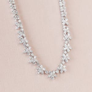 May include: A delicate silver necklace with a floral design made of sparkling clear stones.