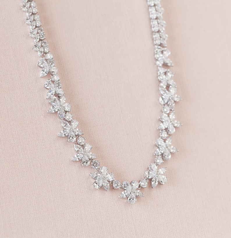 May include: A delicate silver necklace with a floral design made of sparkling clear stones.