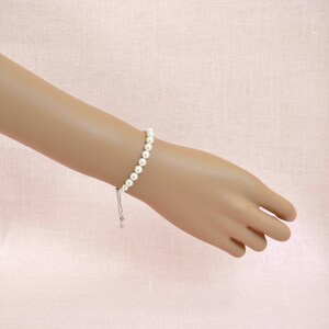 May include: A white pearl bracelet with a silver adjustable clasp. The bracelet is made of small, round pearls and has a simple, elegant design.