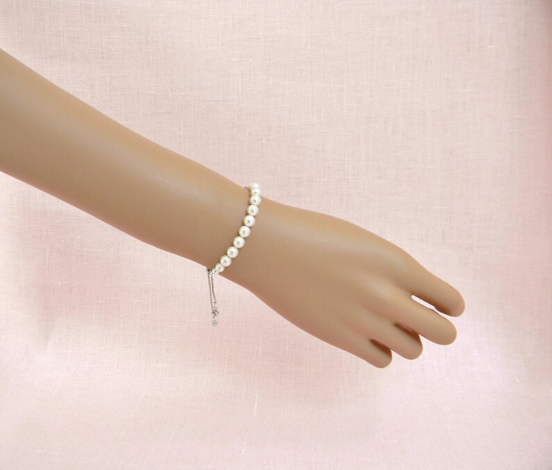 May include: A white pearl bracelet with a silver adjustable clasp. The bracelet is made of small, round pearls and has a simple, elegant design.