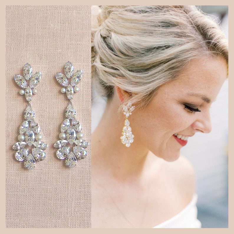May include: A pair of long, crystal and pearl bridal earrings. The earrings are made of clear crystals and white pearls, and they are hanging from a gold hook. The earrings are about 3 inches long.