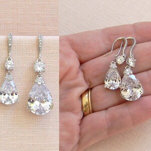 May include: A pair of silver teardrop earrings with clear crystal stones. The earrings have a smaller crystal stone above the larger teardrop stone.