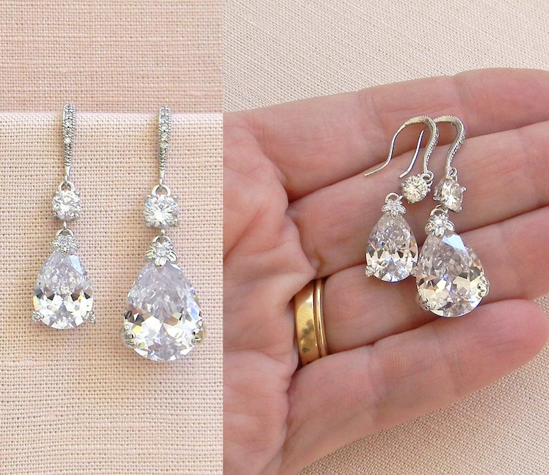 May include: A pair of silver teardrop earrings with clear crystal stones. The earrings have a smaller crystal stone above the larger teardrop stone.