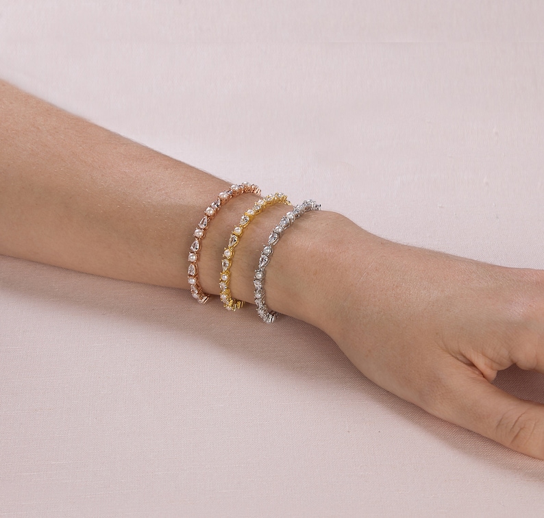 May include: Three delicate bracelets with a row of pear-shaped clear stones set in gold, rose gold, and silver.