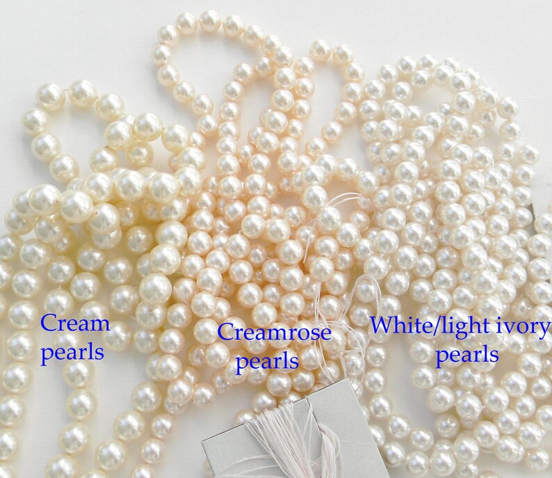May include: Three strands of faux pearl beads in cream, creamrose, and white/light ivory colors. The beads are all the same size and are arranged in a loose pile.