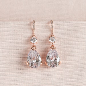 May include: Rose gold dangle earrings with clear pear-shaped and round cubic zirconia stones.