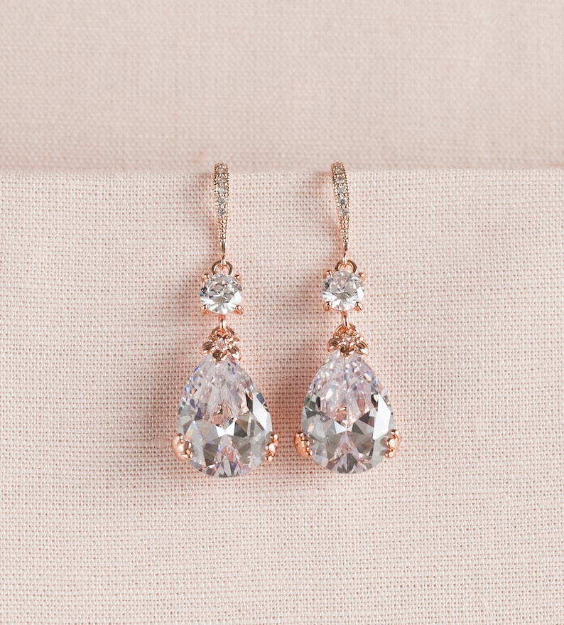 May include: Rose gold dangle earrings with clear pear-shaped and round cubic zirconia stones.