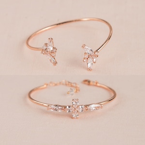 May include: Two rose gold bracelets with clear crystal accents. One bracelet features a delicate floral design, while the other has a cross design.