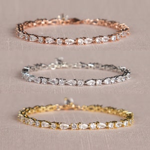 Op de afbeelding: Drie delicate armbanden met peervormige, heldere stenen gezet in zilver, goud en ros&eacute;goud.