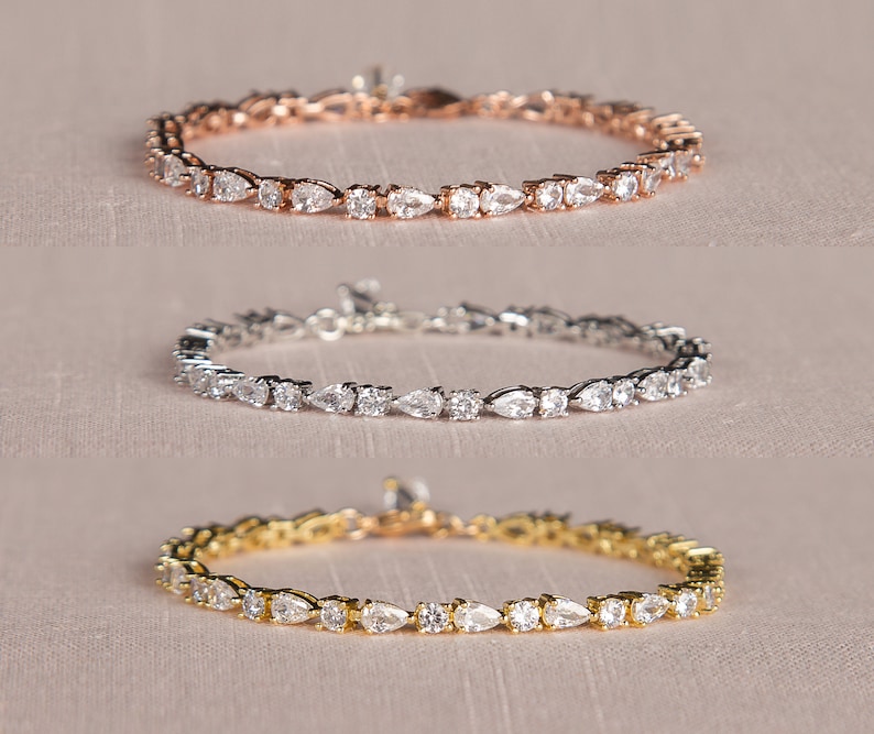 Op de afbeelding: Drie delicate armbanden met peervormige, heldere stenen gezet in zilver, goud en ros&eacute;goud.
