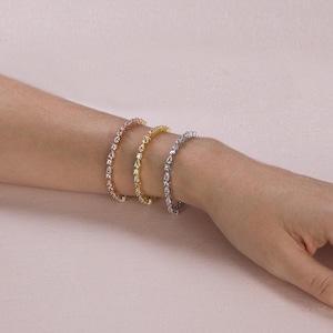 Op de afbeelding: Drie armbanden in zilver, goud en ros&eacute;goud met heldere, peervormige stenen.