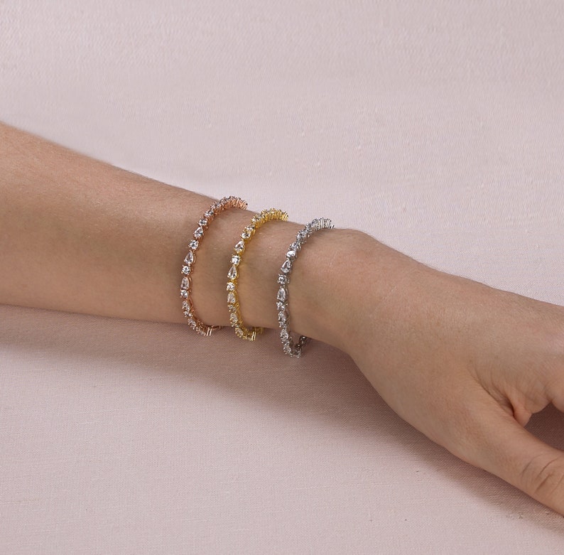 Op de afbeelding: Drie armbanden in zilver, goud en ros&eacute;goud met heldere, peervormige stenen.