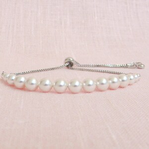 May include: A white pearl bracelet with a silver chain and adjustable clasp. The bracelet is made of small, round pearls and has a simple, elegant design.