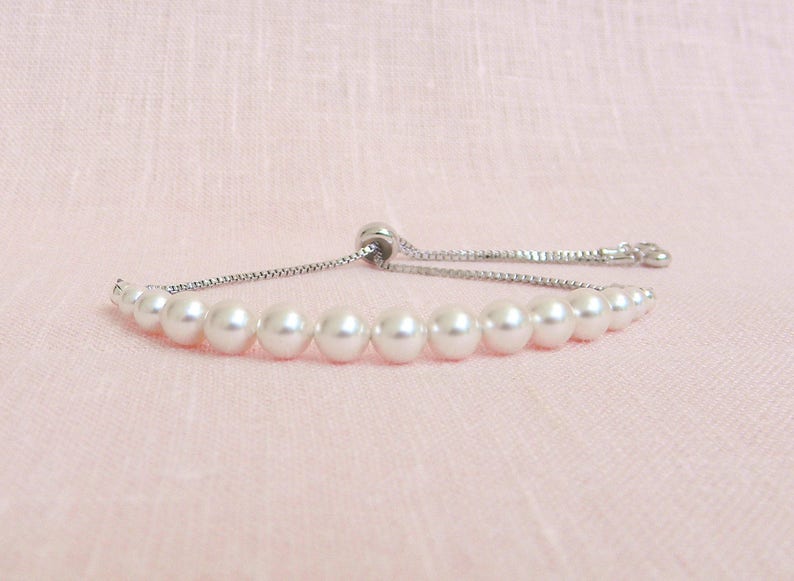May include: A white pearl bracelet with a silver chain and adjustable clasp. The bracelet is made of small, round pearls and has a simple, elegant design.