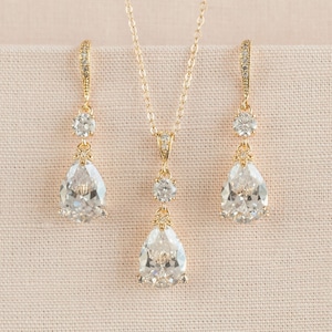 May include: A gold necklace and earrings set with teardrop-shaped clear crystals and smaller round crystals.