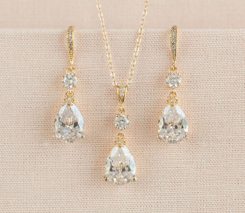 May include: A gold necklace and earrings set with teardrop-shaped clear crystals and smaller round crystals.