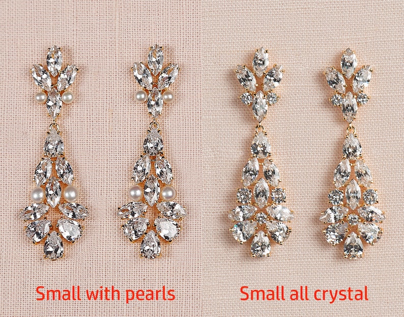 May include: Two pairs of gold dangle earrings with crystal and pearl accents. The earrings on the left have pearls, while the earrings on the right are all crystal. The earrings are labeled "Small with pearls" and "Small all crystal".