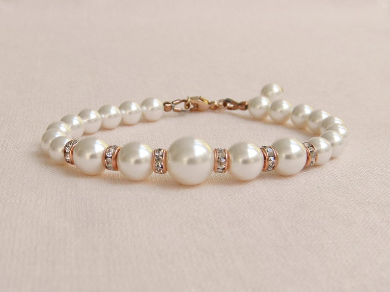 May include: A white pearl bracelet with rose gold accents and clear crystal embellishments.