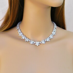 May include: A silver necklace with a delicate design of small, clear rhinestones arranged in a floral pattern. The necklace is worn on a model with brown hair.