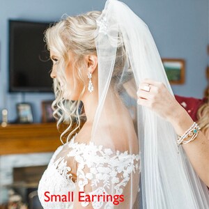 May include: A bride wearing a white wedding dress with a lace bodice and a long white veil. She is wearing small earrings.