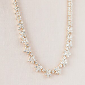 May include: A gold necklace with a delicate design featuring clusters of clear cubic zirconia stones arranged in a floral pattern.