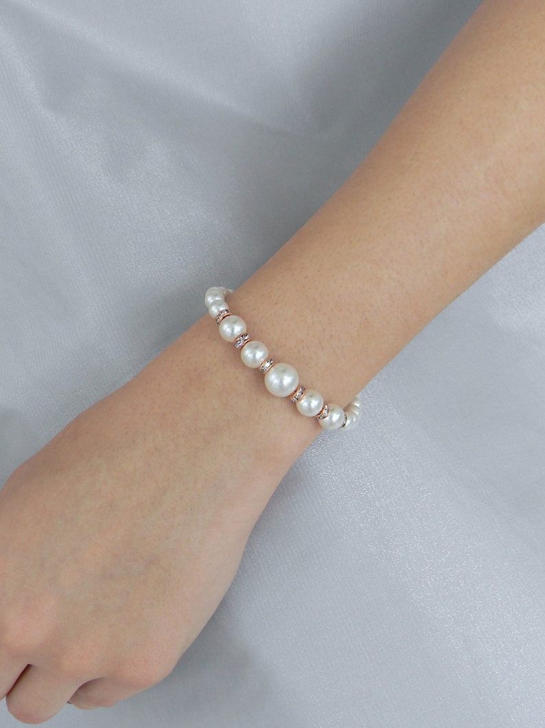 May include: A white pearl bracelet with small clear rhinestones on a rose gold chain.