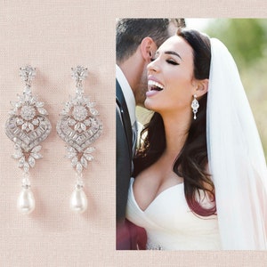 May include: Elegant silver-toned chandelier earrings with intricate crystal detailing and a pear-shaped pearl drop. The earrings are displayed on a light pink background, with a bride wearing similar earrings in the background.