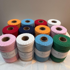 Puede incluir: Una colección de carretes de hilo de macramé de colores, incluyendo rosa, blanco, azul y verde. Cada carrete está etiquetado con texto en un idioma extranjero. Los carretes están dispuestos en filas, mostrando la gama de colores disponibles.