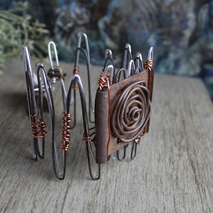 May include: A silver and copper wire bracelet with a brown leather and copper wire rose design.