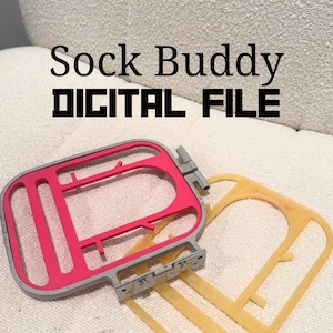 May include: A pink and grey embroidery hoop with a yellow plastic template, labelled "Sock Buddy DIGITAL FILE" in black text. The items are on a textured, off-white surface.
