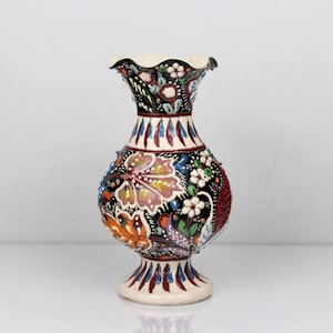 May include: A ceramic vase with a cream-colored base and rim, featuring a bulbous body and a ruffled top. The vase is adorned with colorful floral patterns in shades of orange, pink, blue, and white against a black background. The vase measures approximately 8 inches tall.