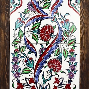 May include: A framed decorative tile panel featuring a floral design. The artwork showcases red, blue, green, and purple flowers and foliage against a white background. The frame is made of dark brown wood, adding a rustic touch.