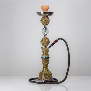 May include: A decorative hookah with a silver metal tray, a ceramic bowl, and a multi-colored beaded design. The hookah has a clear crystal accent and a black hose with a red mouthpiece. The base is also decorated with colorful beads.