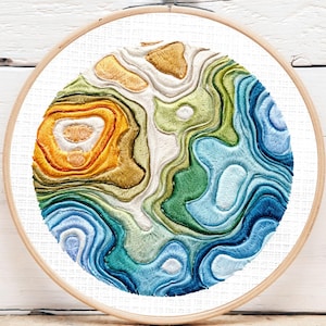 May include: Embroidered artwork in a wooden hoop. The design features a colorful topographic map with shades of blue, green, yellow, and orange. The text "Digital Download (PDF)" is in a blue circle in the upper left corner.