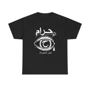 May include: Black t-shirt with a white graphic design. The design features an eye with a stylized tear and Arabic text above and below the eye. The shirt is a crew neck and appears to be made of cotton.